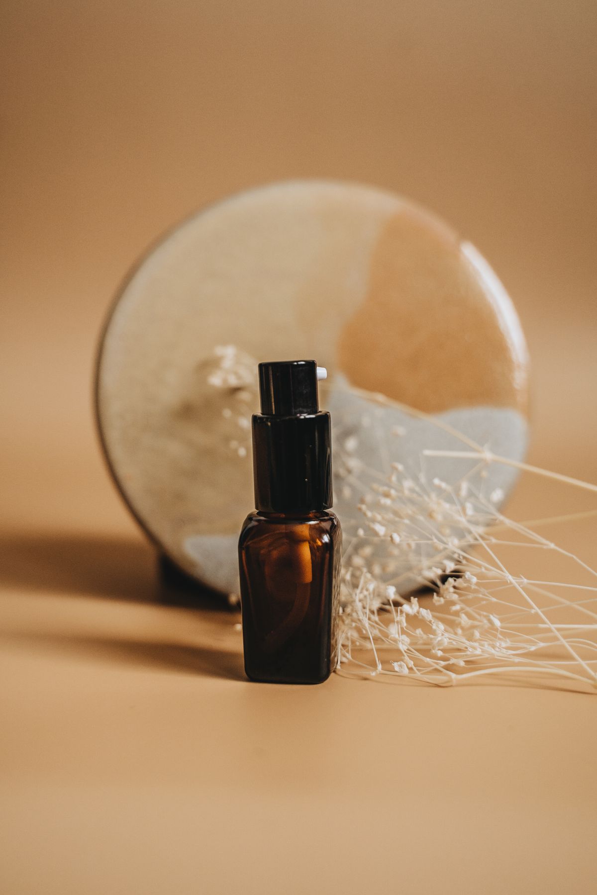 Amber serum bottle and dried flowers on a warm background